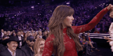 A Woman In A Red Lace Top Stands In Front Of A Crowd GIF