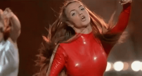 A Woman In A Red Latex Top Is Dancing On A Stage With Her Hair Blowing In The Wind . GIF