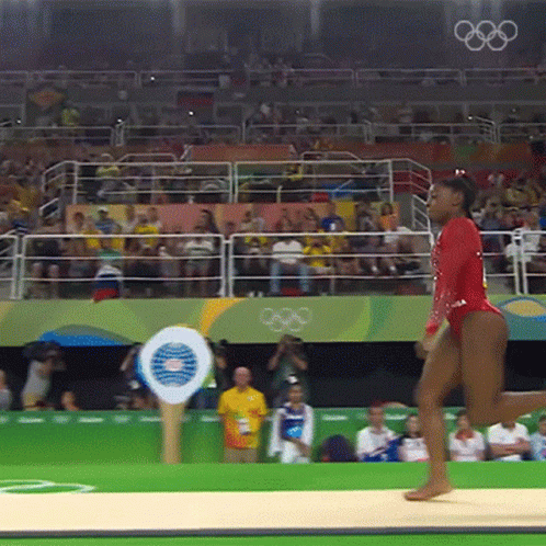 A Woman In A Red Leotard Is Doing A Routine In Front Of A Crowd That Is Watching The Olympics GIF