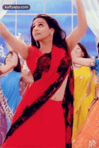 A Woman In A Red Saree Is Dancing In Front Of A Group Of Women In Different Colored Dresses . GIF