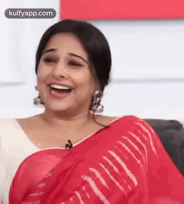 A Woman In A Red Saree Is Laughing While Sitting On A Chair . GIF