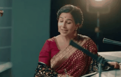 A Woman In A Red Saree Is Sitting In Front Of A Microphone And Says It Would Be My Absolute Pleasure . GIF