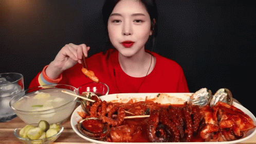 A Woman In A Red Shirt Is Eating A Large Plate Of Food With Chopsticks GIF