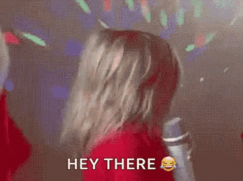 A Woman In A Red Shirt Is Holding A Microphone And Says Hey There . GIF