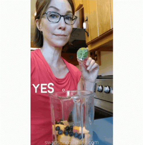 A Woman In A Red Shirt Is Holding A Piece Of Fruit In Front Of A Blender That Says Yes GIF