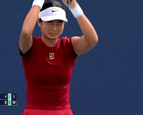 A Woman In A Red Shirt Is Holding A Tennis Racquet In Her Hand GIF