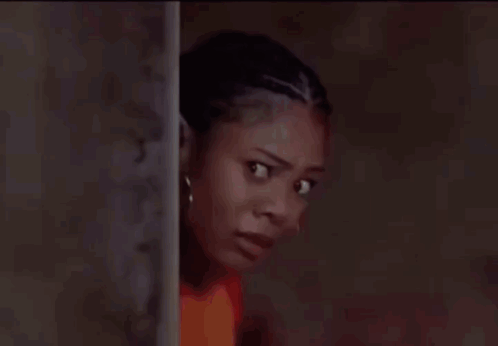 A Woman In A Red Shirt Is Leaning Against A Wall And Looking At The Camera . GIF