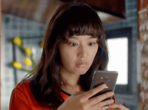 A Woman In A Red Shirt Is Looking At A Cell Phone GIF