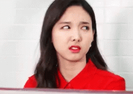 A Woman In A Red Shirt Is Making A Funny Face And Looking At The Camera . GIF