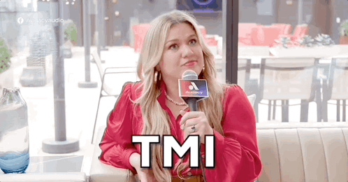 A Woman In A Red Shirt Is Sitting At A Table Holding A Microphone And Says Tmi . GIF