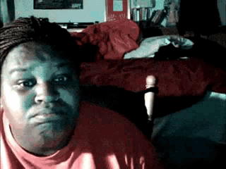 A Woman In A Red Shirt Is Sitting In Front Of A Bed With A Red Blanket On It GIF
