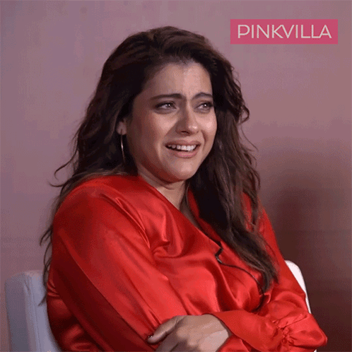 A Woman In A Red Shirt Is Sitting In Front Of A Pink Wall With Pinkvilla Written On It GIF