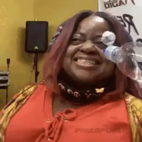 A Woman In A Red Shirt Is Smiling And Holding A Bottle Of Water In Front Of Her Face . GIF