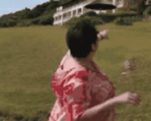 A Woman In A Red Shirt Is Standing In A Field Pointing At Something . GIF