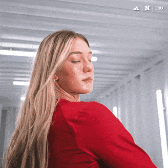 a woman in a red shirt is standing in a hallway with the adidas logo on the bottom left
