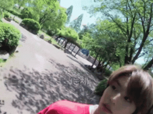 A Woman In A Red Shirt Is Standing In A Park GIF