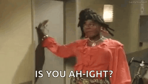 a woman in a red shirt is standing in front of a door and asking , `` is you ah-ight ? ''