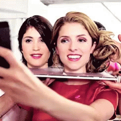 A Woman In A Red Shirt Is Taking A Selfie With Another Woman Behind Her . GIF