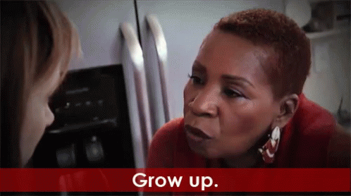 A Woman In A Red Shirt Is Talking To Another Woman In Front Of A Refrigerator And The Words Grow Up Are On The Bottom GIF