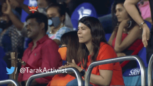 A Woman In A Red Shirt Sits In A Stadium With A Twitter / @Tarakactivist Written Below Her GIF