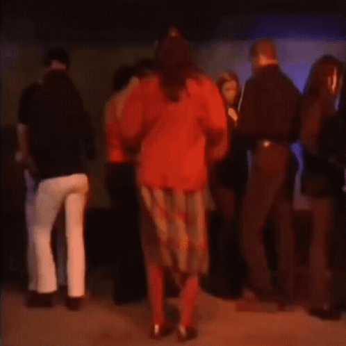 A Woman In A Red Sweater Is Dancing With A Group Of People GIF