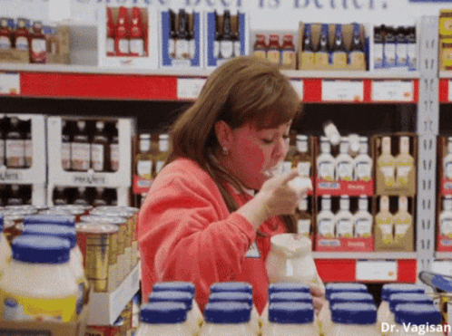 A Woman In A Red Sweater Is Drinking From A Pitcher In A Store GIF