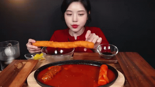 A Woman In A Red Sweater Is Eating A Large Piece Of Food GIF