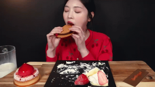 A Woman In A Red Sweater Is Eating A Sandwich With Strawberries On It GIF