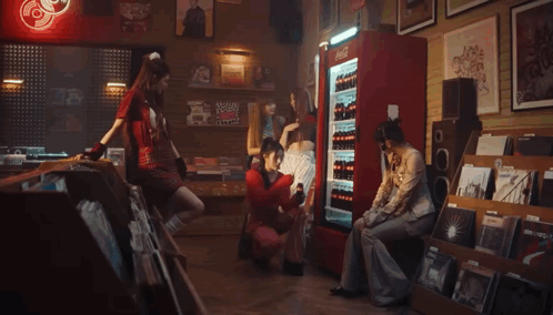 A Woman In A Red Sweater Is Holding A Bottle Of Coca Cola In Front Of A Refrigerator . GIF