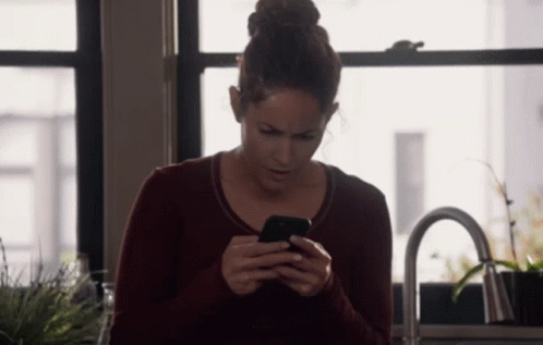 A Woman In A Red Sweater Is Looking At Her Phone GIF