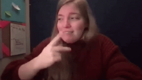 A Woman In A Red Sweater Is Making A Funny Face While Sitting At A Table . GIF