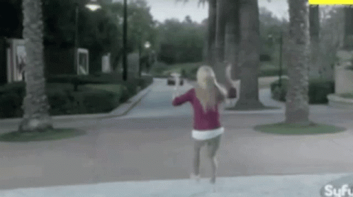 A Woman In A Red Sweater Is Running Down A Sidewalk . GIF