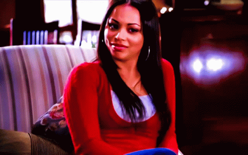 A Woman In A Red Sweater Is Sitting On A Couch And Smiling GIF