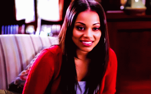 A Woman In A Red Sweater Is Smiling And Looking At The Camera GIF