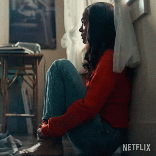 A Woman In A Red Sweater Sits On The Floor In Front Of A Netflix Sign GIF