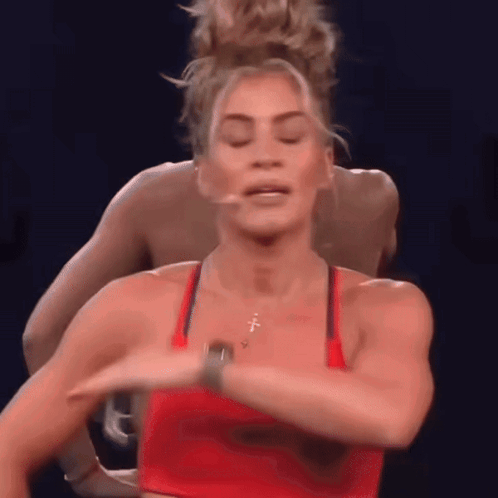 A Woman In A Red Tank Top Is Dancing With A Man In A Blue Shirt Behind Her . GIF