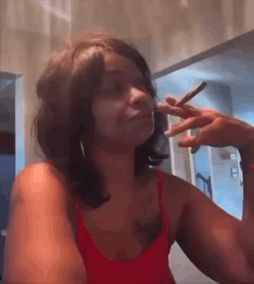 A Woman In A Red Tank Top Is Smoking A Cigarette In A Bathroom . GIF