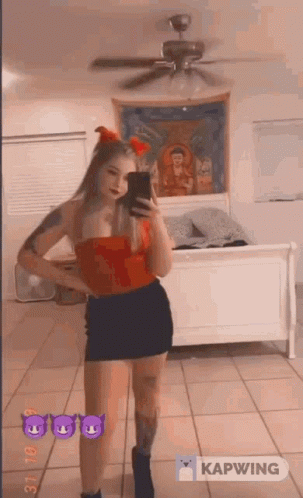 A Woman In A Red Top And Black Skirt Is Taking A Picture Of Herself In A Mirror . GIF