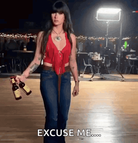 A Woman In A Red Top And Blue Jeans Is Holding Two Bottles Of Wine And Says Excuse Me GIF
