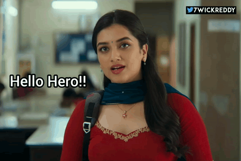 A Woman In A Red Top And Blue Scarf Is Standing In A Hallway And Says Hello Hero GIF
