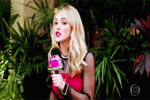 a woman in a red top is holding a microphone in front of plants