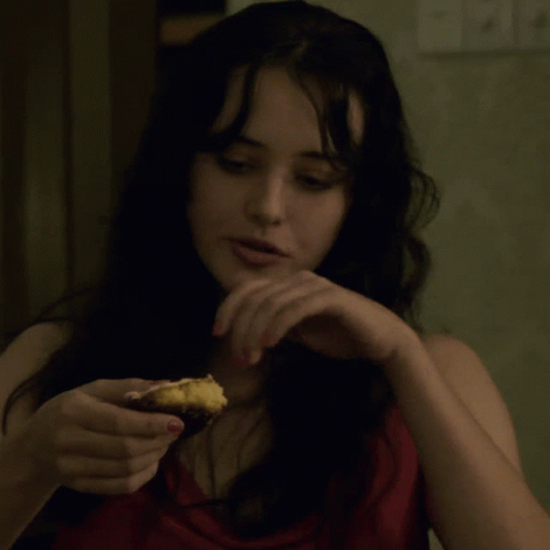 a woman in a red top is holding a piece of food in her hand