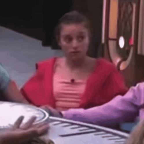 a woman in a red top is sitting at a table with a clock on it .