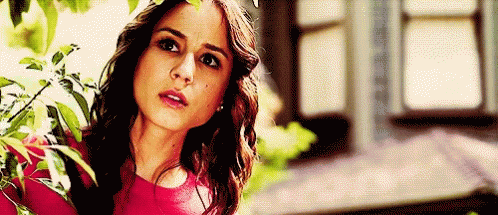 A Woman In A Red Top Is Standing In Front Of A Window . GIF