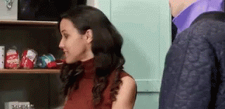 A Woman In A Red Top Is Standing Next To A Man In A Purple Shirt In A Kitchen . GIF