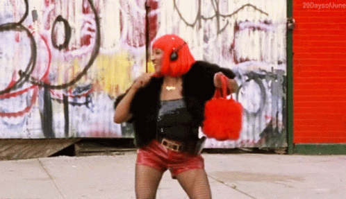 A Woman In A Red Wig And Red Shorts Is Dancing In Front Of A Graffiti Wall With The Words 20Daysofjune Below Her GIF
