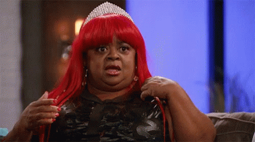 A Woman In A Red Wig And Tiara Is Sitting On A Couch . GIF