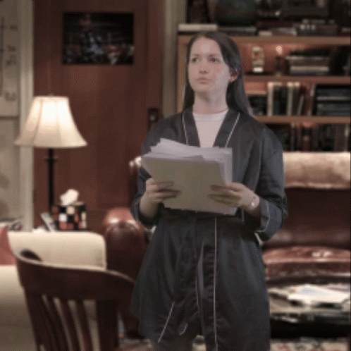 A Woman In A Robe Holds A Piece Of Paper In Her Hands GIF