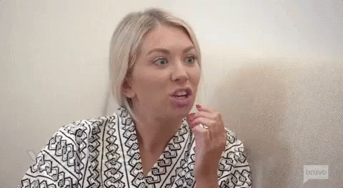A Woman In A Robe Is Sitting On A Couch And Making A Funny Face . GIF