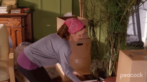 A Woman In A Room With Boxes And A Peacock Logo On The Bottom Right GIF